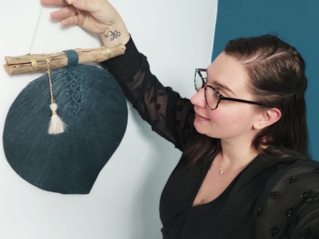 Cliente souriante tenant une décoration murale personnalisée en fibres naturelles et bois flotté