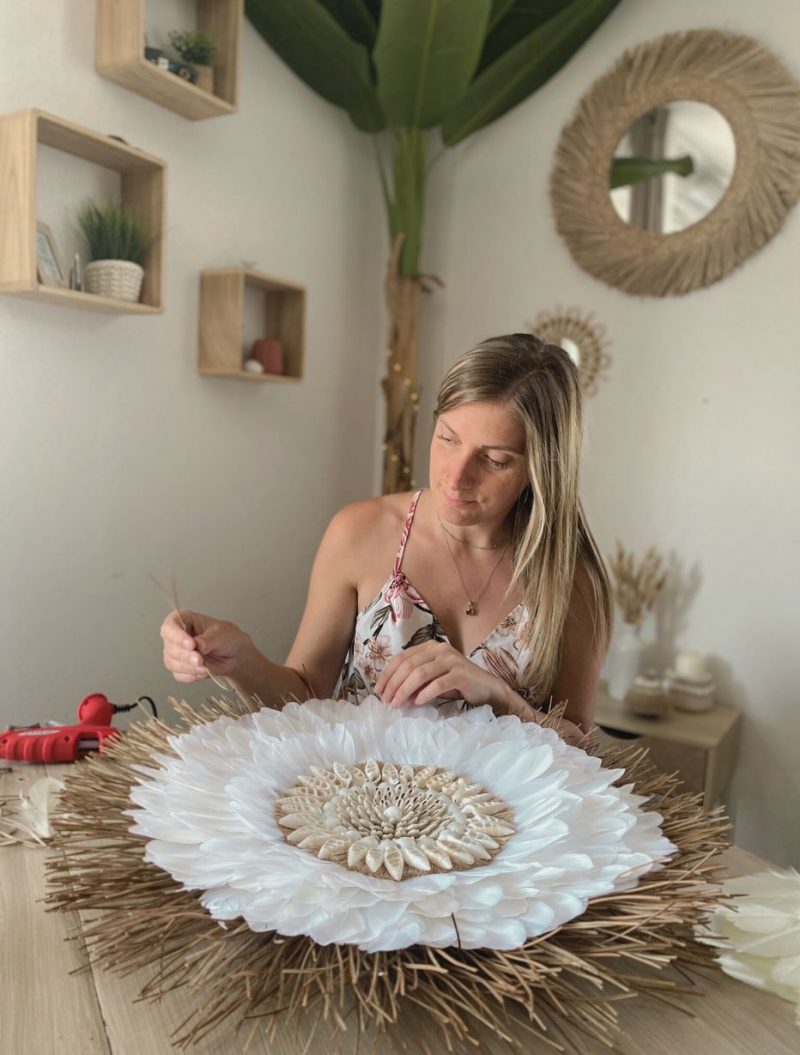 Artisane en train de créer un juju hat blanc bohème en plumes, aiguilles de pin, coquillages et jute
