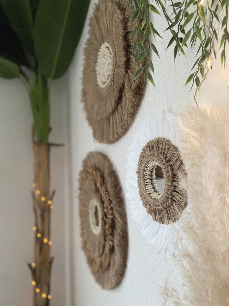 Trois miroirs muraux ronds faits main en jute et plumes, accrochés sur un mur blanc dans une décoration naturelle. Création personnalisée bohème