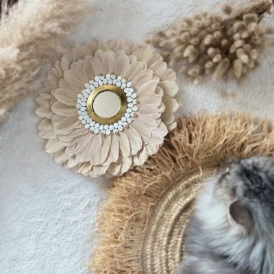 Juju hat bohème en plumes beige et blanc entouré de décoration naturelle. Décoration artisanale