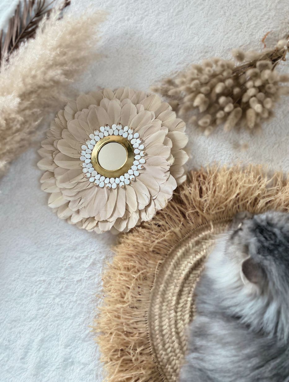Juju hat bohème en plumes beige et blanc entouré de décoration naturelle. Décoration artisanale