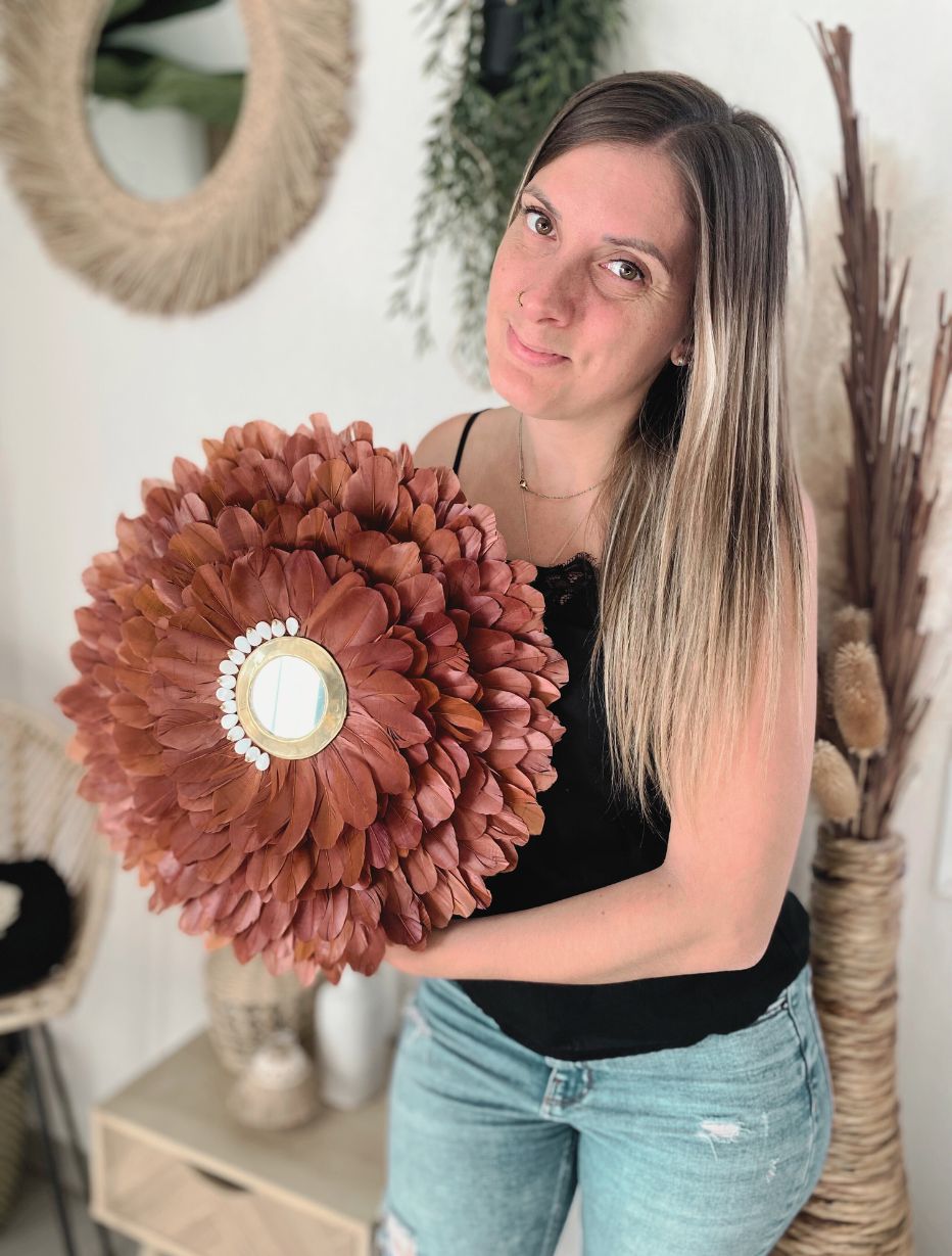 Créatrice tenant un miroir juju hat coquillages et plumes naturelles couleur terracotta, décoration murale artisanale